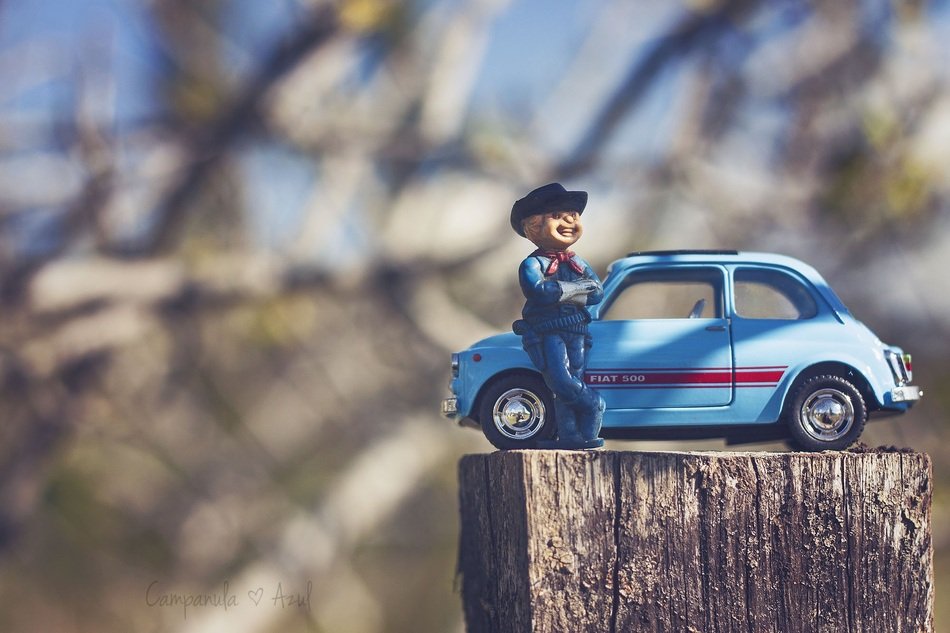 Man figure with the blue car on the wood on blurred background