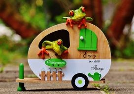 Green frogs in a wooden cart on blurred background with the plants