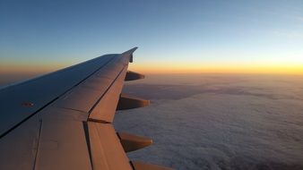 airplane wing above white clouds during sunset