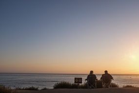 man and woman sit on beach at sea