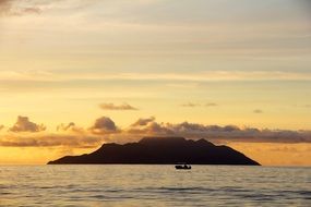 island in the rays of sunset with the boat in front of it