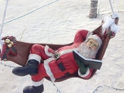 Santa statue reading a book in a hammock on the beach