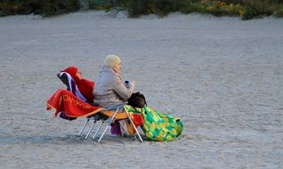 elderly woman sits on a chair on the beach