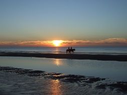 horseback riding on the beach at sunset