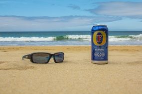 a bottle of beer next to sunglasses on the beach