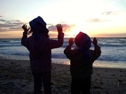 silhouettes of two children on the beach at sunset