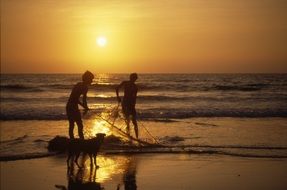 silhouettes of children with a net on the beach at sunset in india