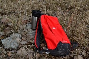 red backpack and thermos on stones among grass