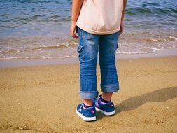 child in blue jeans on a sandy beach