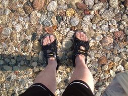 male feet in sandals underwater on the pebbles on a shore