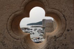 view of boats in harbor through Hole in stone Balustrade, croatia, dubrovnik