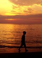 Silhouette of the person walking on the beach at colorful sunset