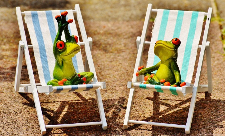 Cure ceramic frogs relax on blue and white sunbeds on the sand