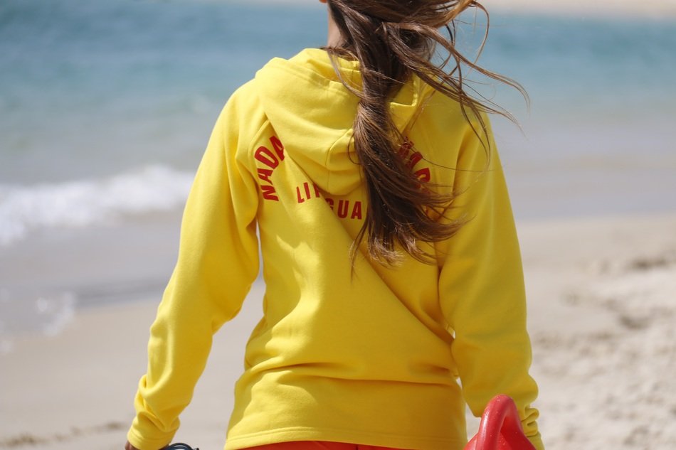 watchful lifeguard in yellow and red sweatshirt on the sandy beach