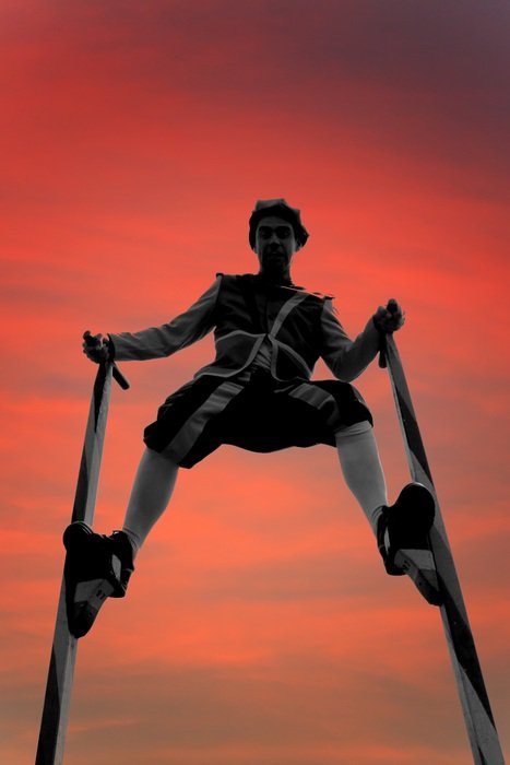 man on stilts against a pink sky