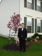 a man in a suit stands near a tree