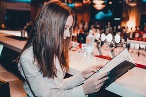woman with brown long hair is studying the menu