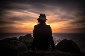 person in hat sitting seaside sunset