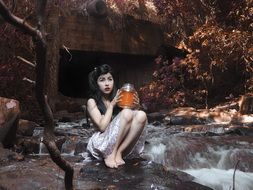 Photo of model sitting on the riverside with glass in her hands