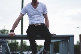 young man in a white t-shirt sits on a wooden pier