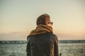 woman in leather jacket sits on the seashore