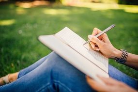 Woman writing notes in notebook at blurred background with grass