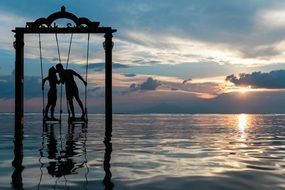 Silhouette of a couple kissing on a swing on a lake at beautiful and colorful sunset