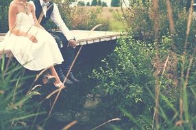 Photo of bride and groom sitting on a bridge