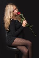 Blonde young woman in black dress with Red rose