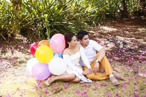 young couple with colorful balloons sitting at ground