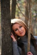 girl in a gray sweater stands by the tree