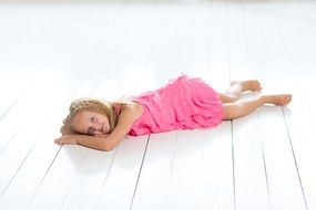 a girl in a pink dress lies on a wooden floor