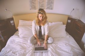 Blonde woman working in bed laptop typing