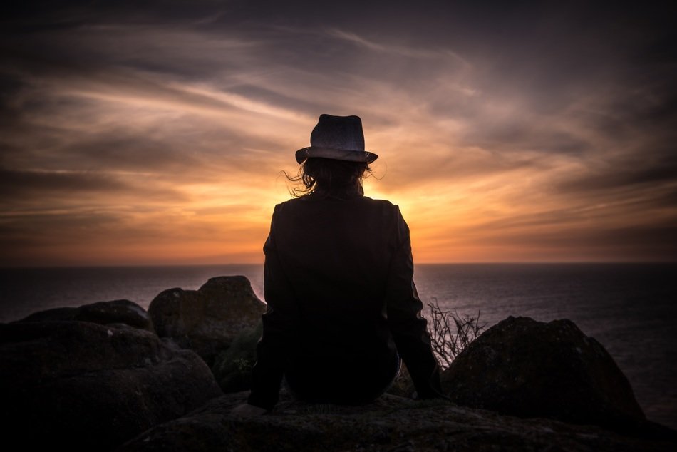person in hat sitting seaside sunset