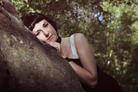 model leaning on stone in a forest