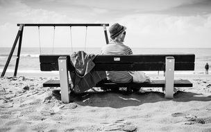 monochrome picture of woman is sitting on a bench on a sand beach