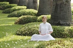 girl in a white suit meditates in a park at Wat Phra Dhammakaya