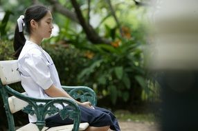 Asian girl meditating on bench in park