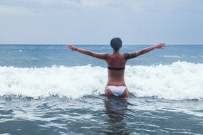 back view of woman standing in water with wide open hands