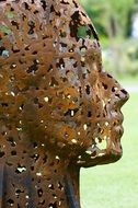 rusty sculpture of a girl with holes on the face