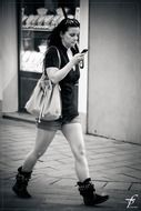black and white photo of a girl walking down the street with a phone in her hand