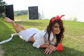 young woman on the grass in a white suit and with a red heart in her hand