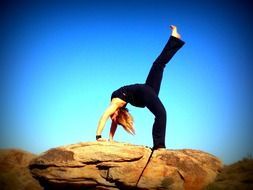 girls in a black suit doing yoga on a rock