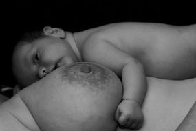 side view of a nude woman's breast with the nipple on the background of a newborn baby