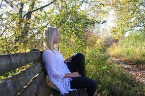 young blonde girl sits on bench at fall, side view