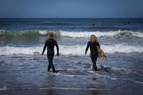 surfers, two women walking through waves