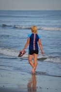view from the back of a woman strolling with a running shoes in her hand