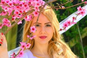 Beauty girl with blond hair on the background of the spring flowering branches of tree