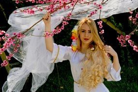 Beauty girl with blond hair on the background of blossoming branches of tree