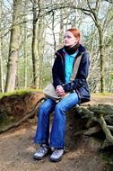 girl is sitting on the root of a tree in the forest
